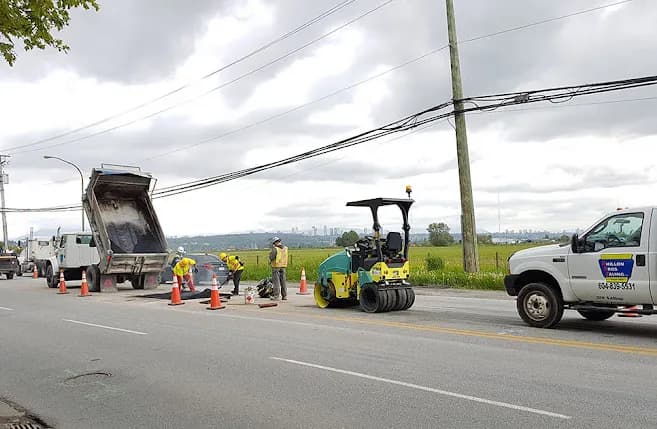 A Dhillon Bros Paving crew resurfacing a road, dump truck and roller working behind traffic cones