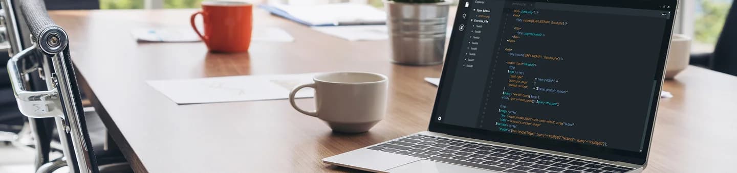 Laptop showing website code on a desk with coffee cups