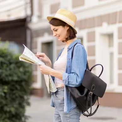 A traveller in a straw hat and backpack reading a folded paper map on a European street.